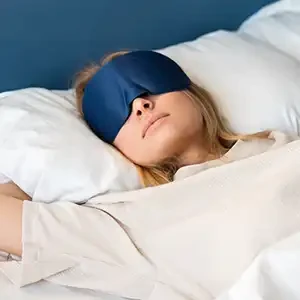 a woman sleeping on a white bad with an eye mask