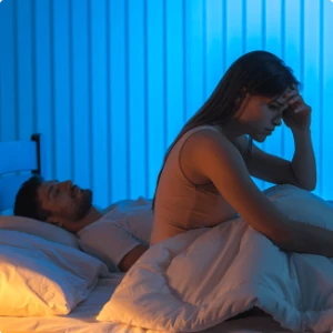 Woman awake, looking upset, while her partner is sleeping. 