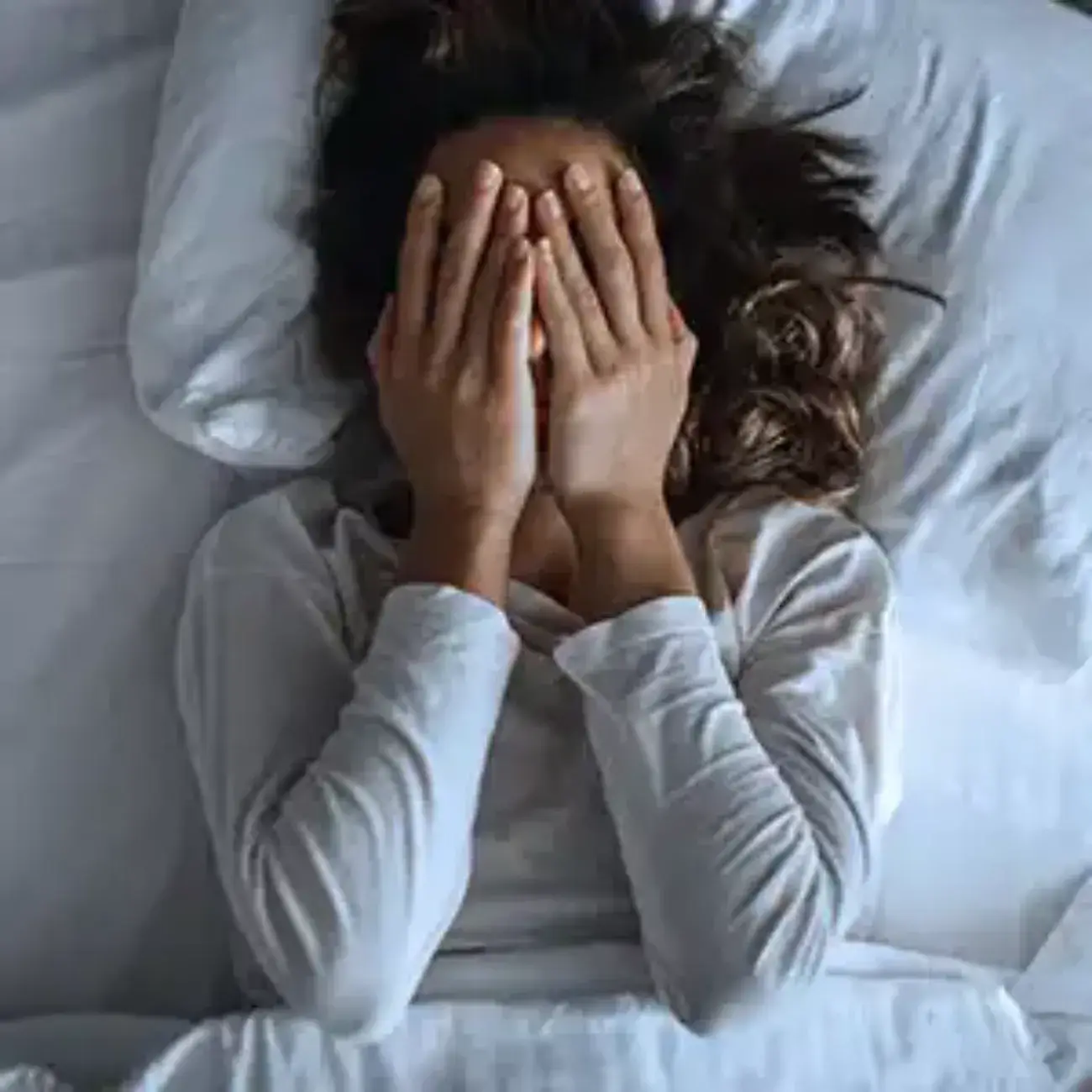 a woman lies in bed with her hands over her face